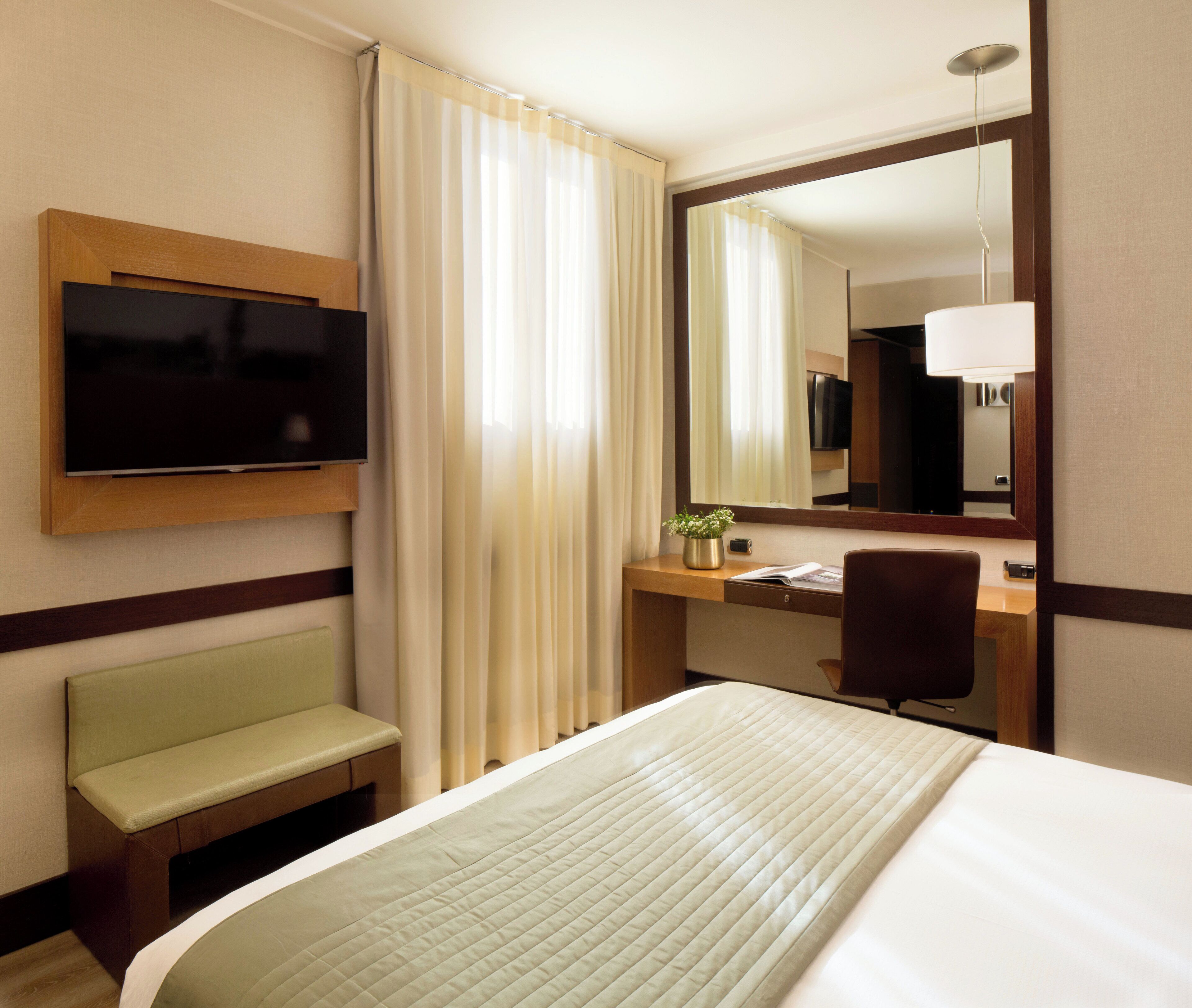 Een hotelkamer met een bed, een bureau, een stoel, een televisie en een spiegel.