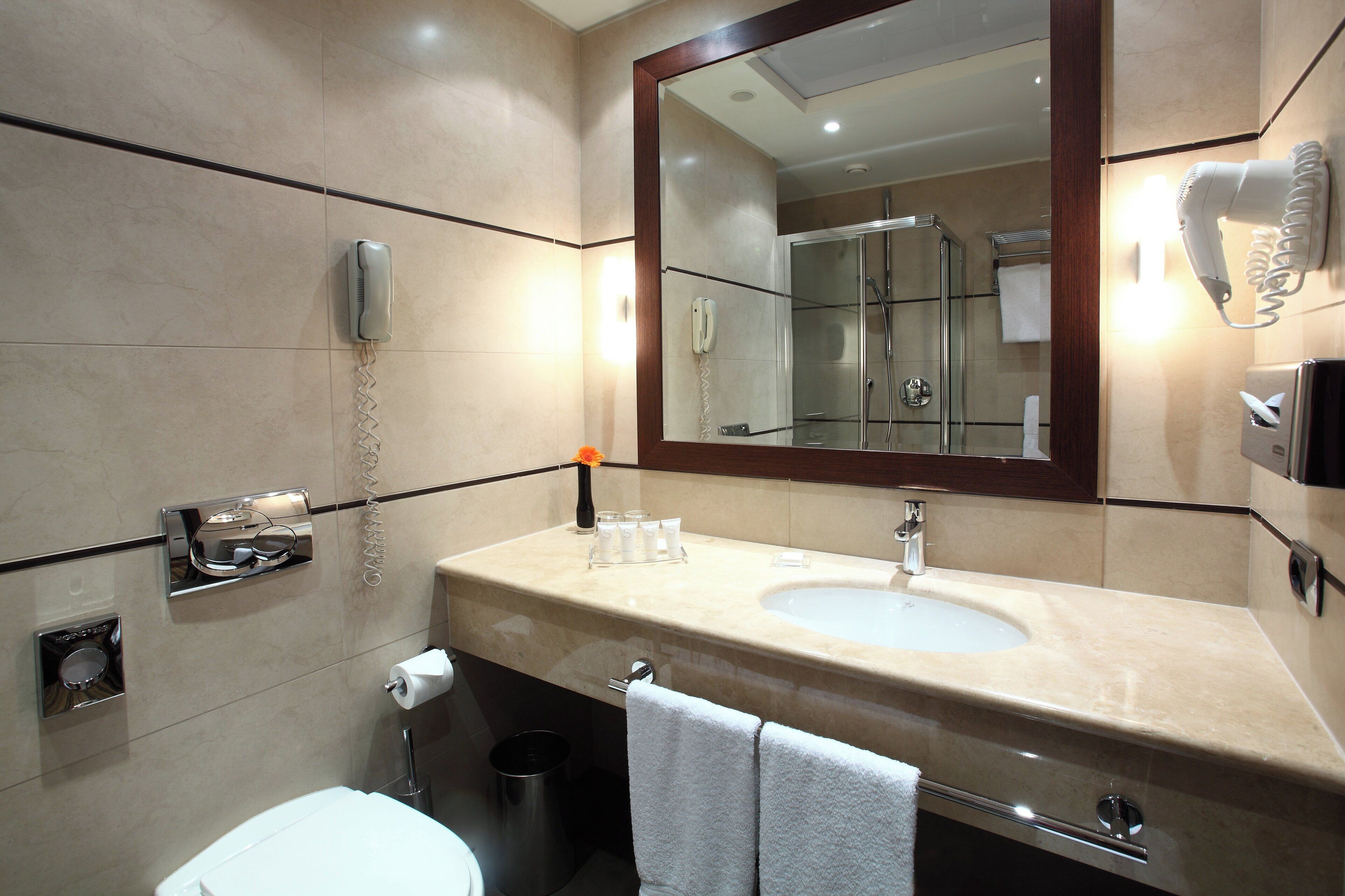 A modern bathroom with a large mirror, a sink, a toilet, and a shower.