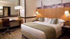 A hotel room with a large bed, a desk with a chair, a mirror, and two bedside lamps.