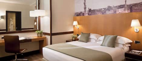 Habitación de hotel con una cama grande, un escritorio con una silla, un espejo y dos lámparas de noche.