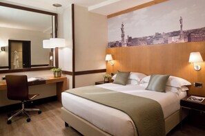 A hotel room with a large bed, a desk with a chair, a mirror, and two bedside lamps.