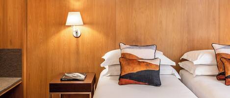 A hotel room with a wooden headboard, a nightstand with a lamp, and two beds with decorative pillows.