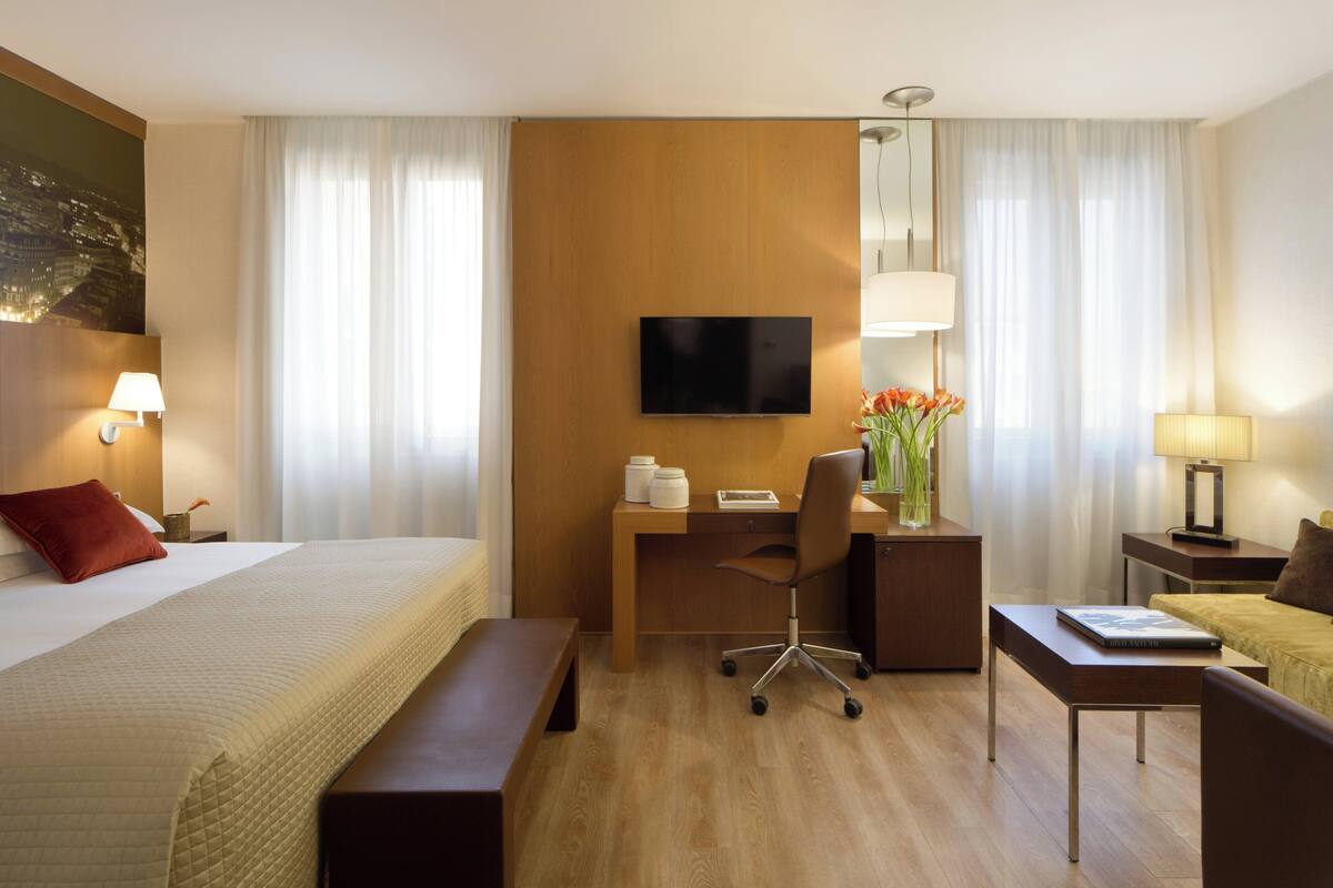 A hotel room with a bed, desk, chair, and a TV mounted on the wall.
