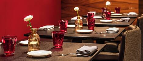 A restaurant setting with tables set for dining, featuring red glassware and a white flower centerpiece.