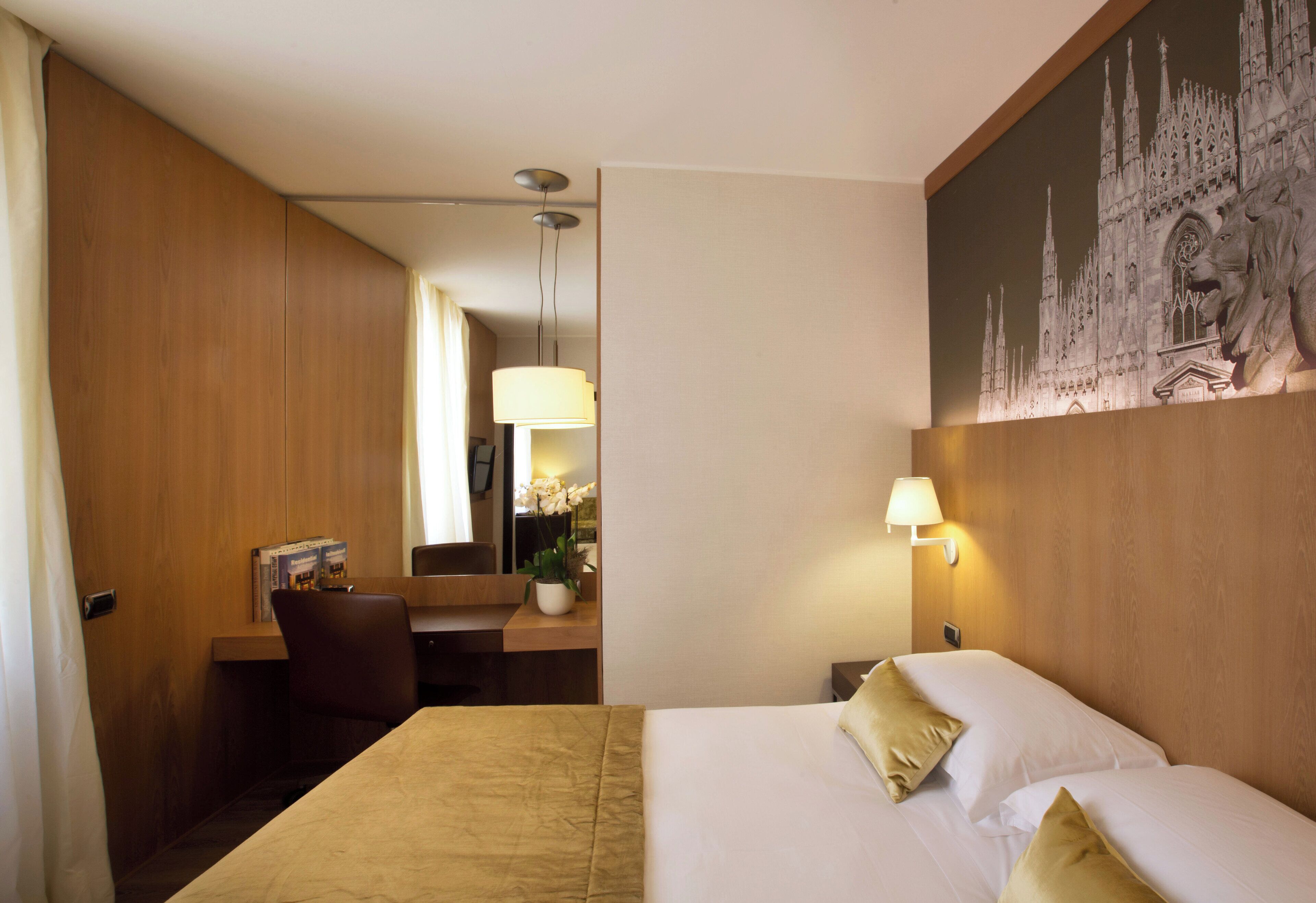 Habitación de hotel con una cama grande, un escritorio con silla, una lámpara y un cuadro en la pared.