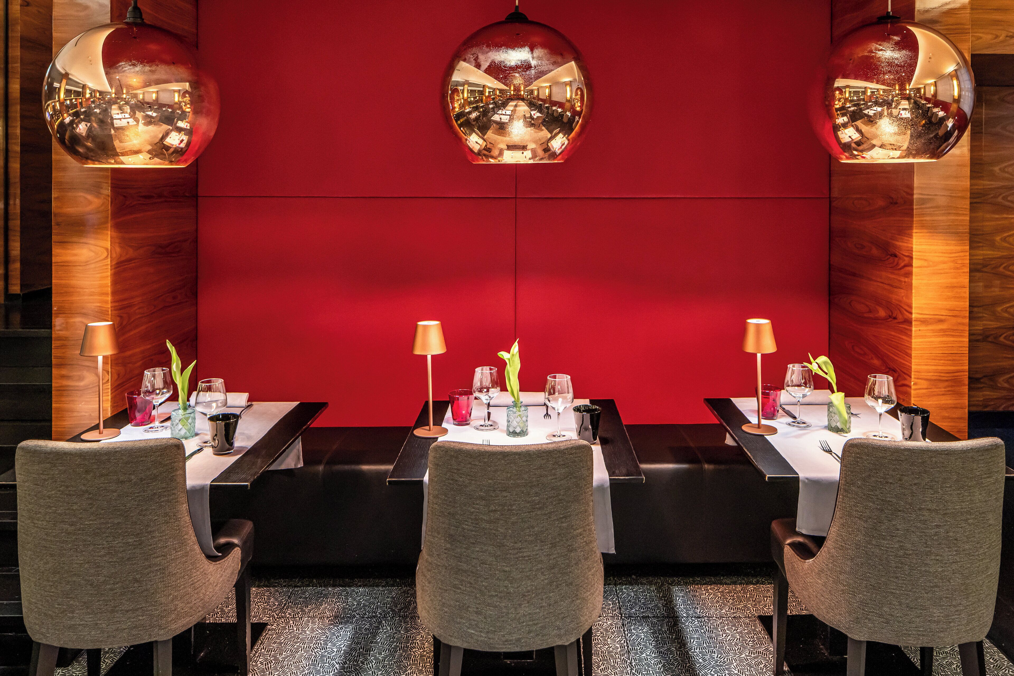 Ein Restaurant mit drei Tischen, an jedem Tisch eine Lampe, eine Pflanze im Blumenvasen und Weingläser.