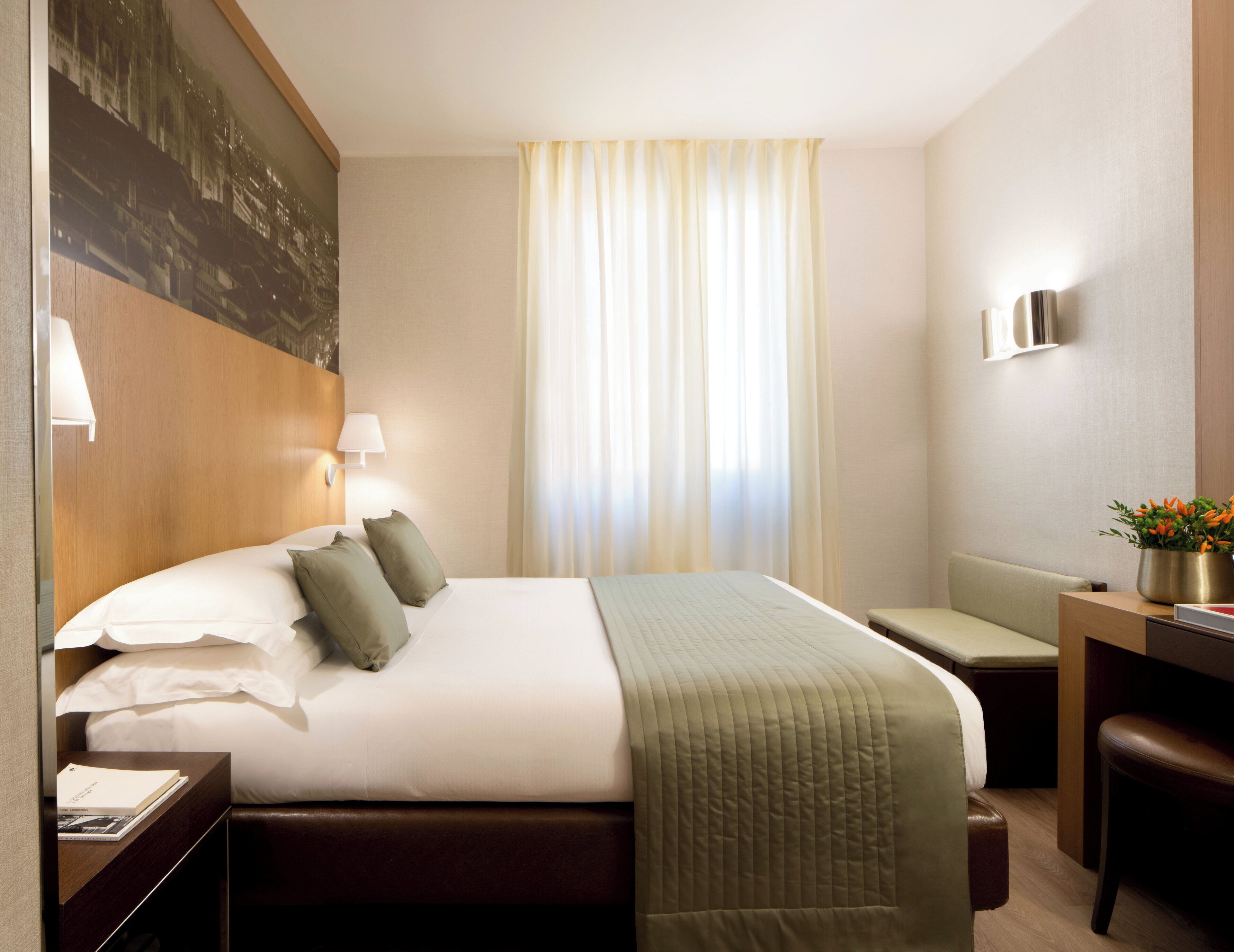A hotel room with a large bed, a desk, a chair, and a window with curtains.