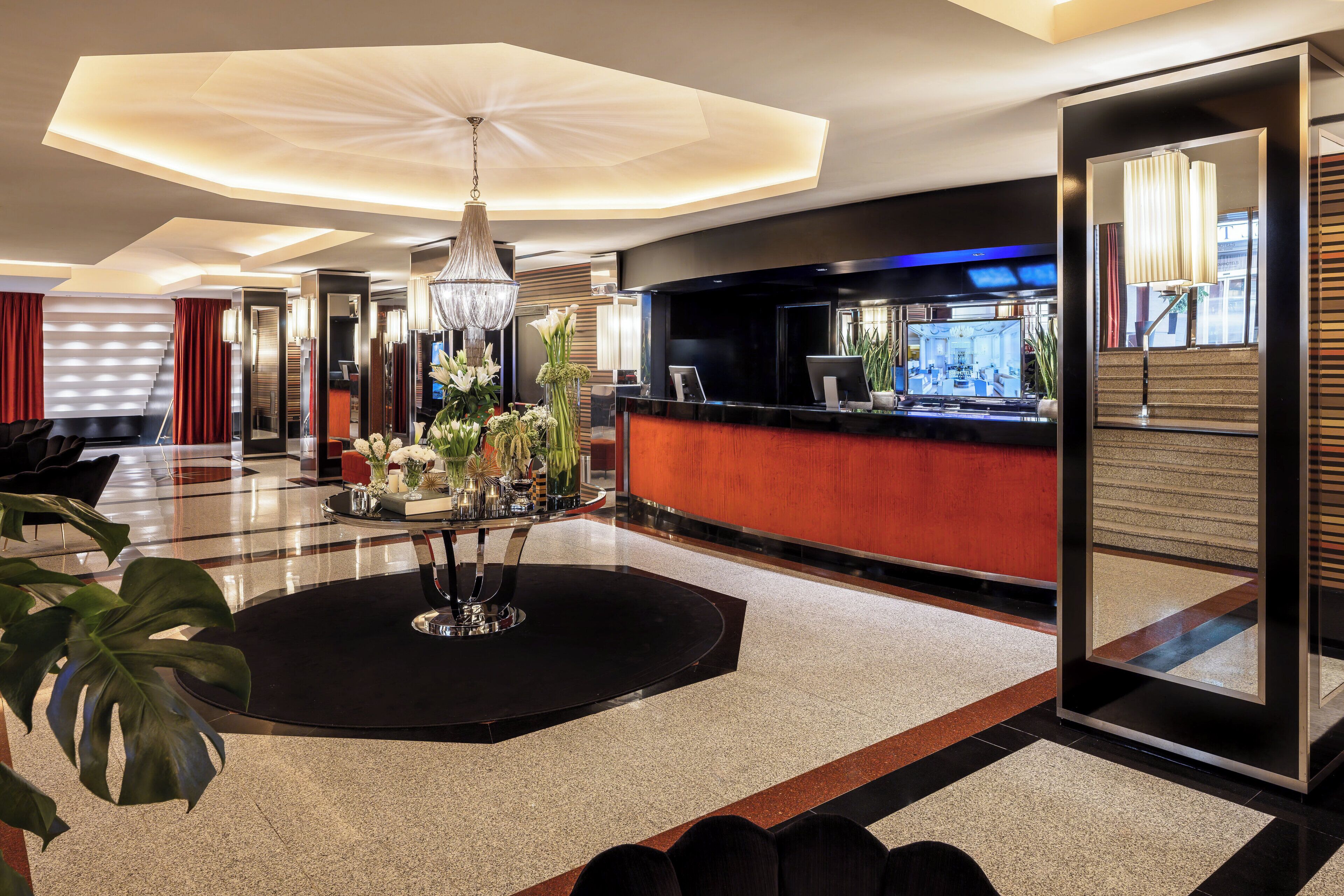 Un moderno vestíbulo de hotel con una recepción, una araña y un espejo grande que refleja el interior.