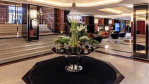 A modern lobby with a central chandelier, a staircase, and a seating area with a TV. - Starhotels Ritz (Milan)