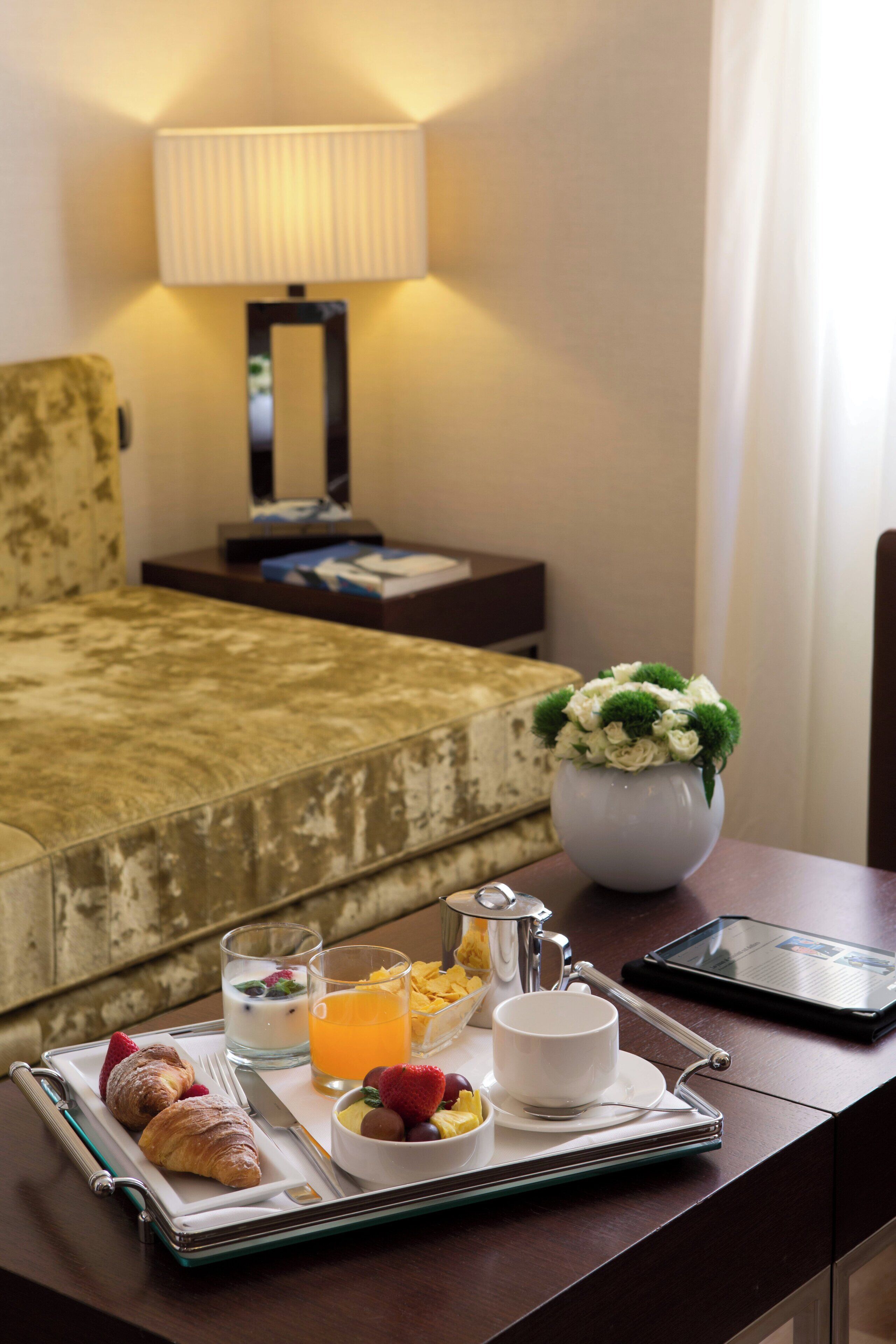 Una bandeja de desayuno ordenada con croissants, frutas y bebidas sobre una mesa de madera en una habitación de hotel.