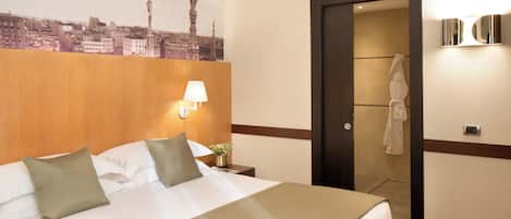Habitación de hotel con cama, mesita de noche, lámpara, espejo y vista del paisaje urbano a través del ventanal.