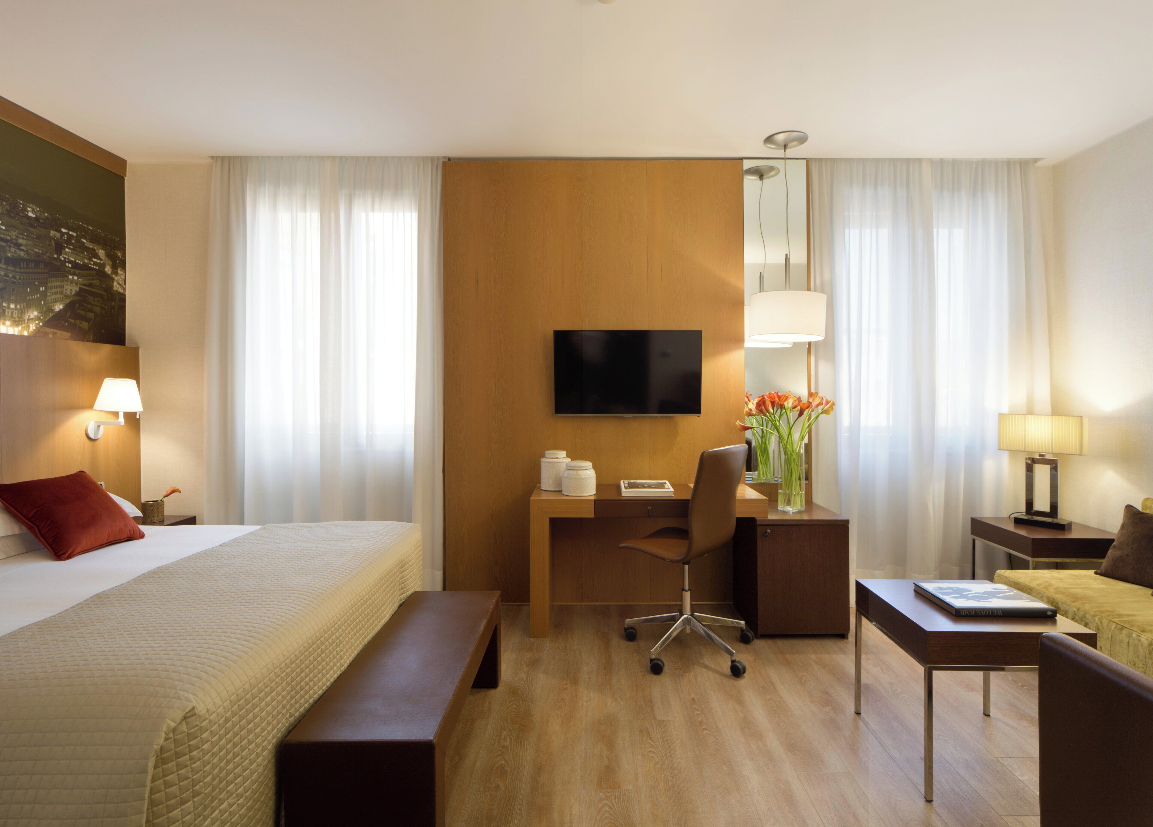 Een hotelkamer met een bed, bureau, stoel en een aan de muur bevestigde televisie.