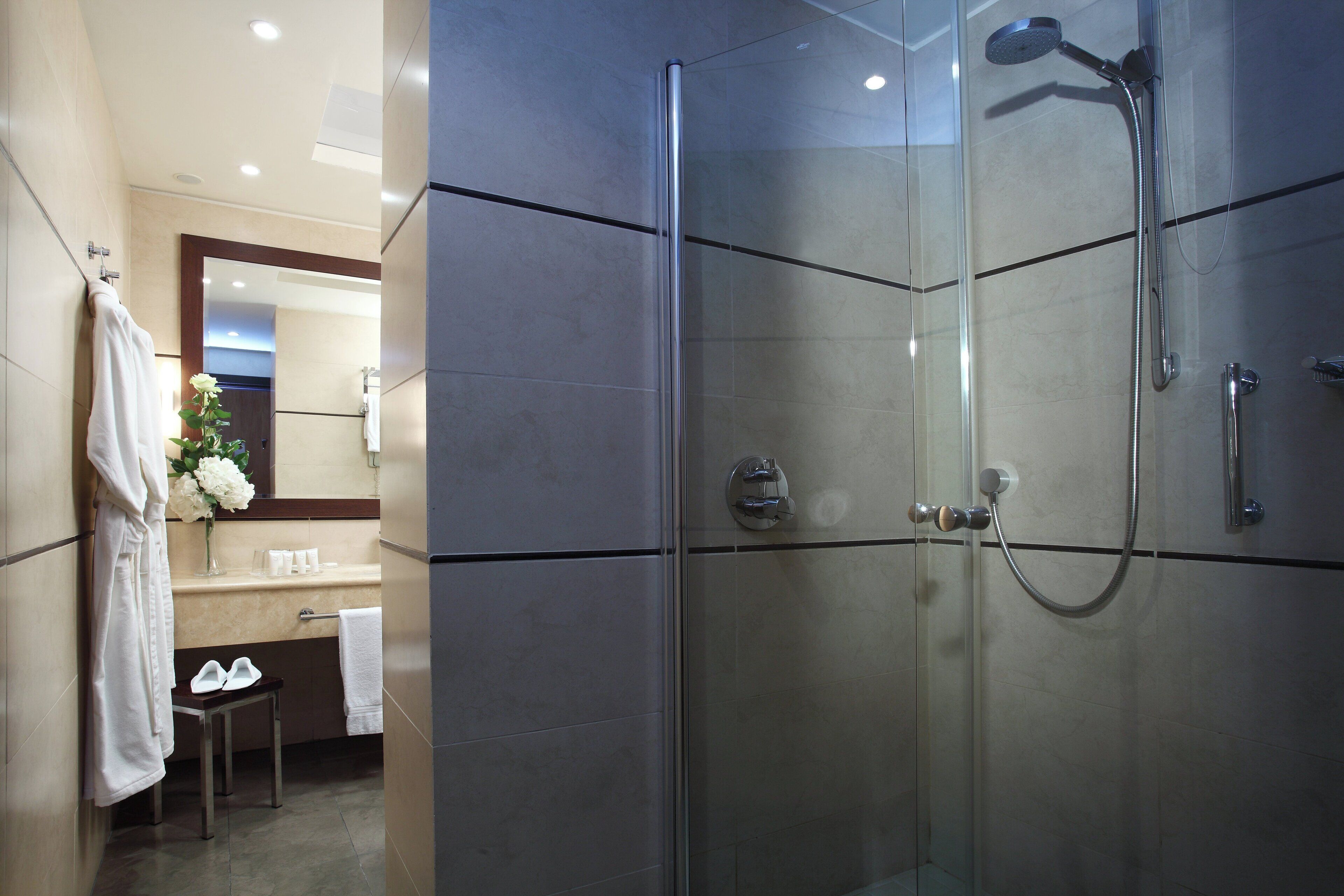 A modern bathroom with a glass-enclosed shower, a vanity with a mirror, and a small stool with shoes on it.