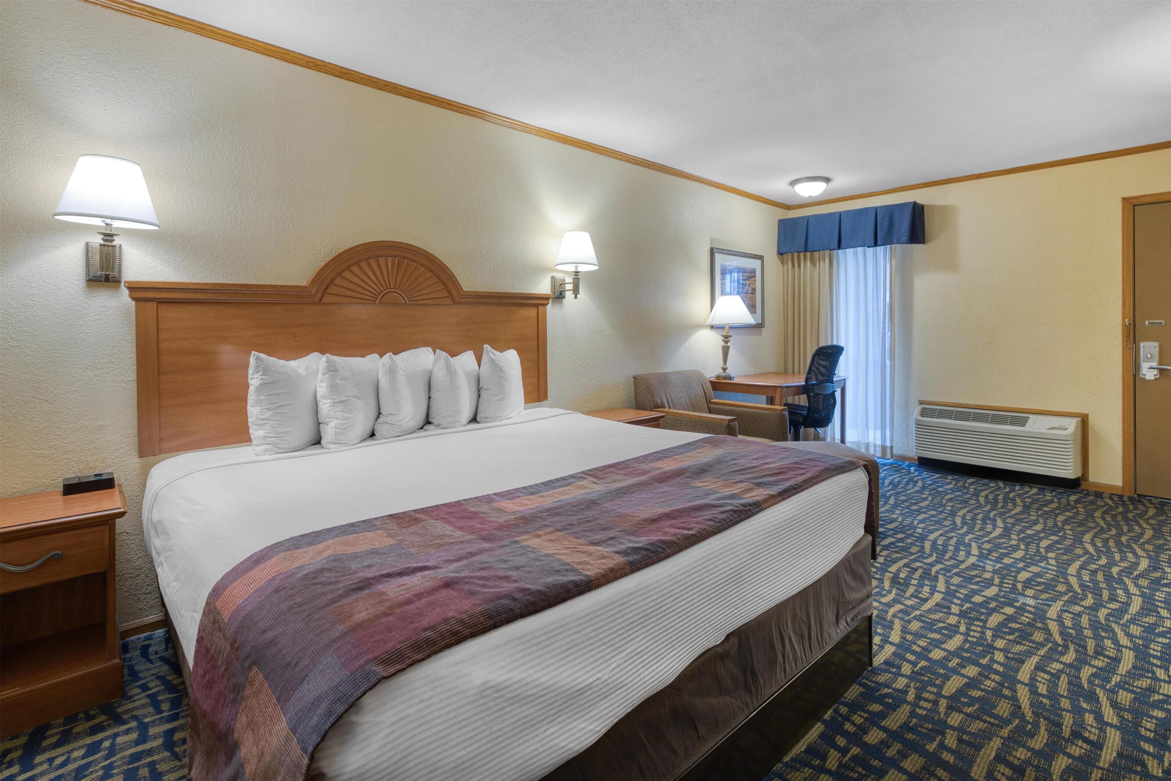 Une chambre d’hôtel avec un grand lit, deux tables de chevet, un bureau, une chaise et une fenêtre avec des rideaux.