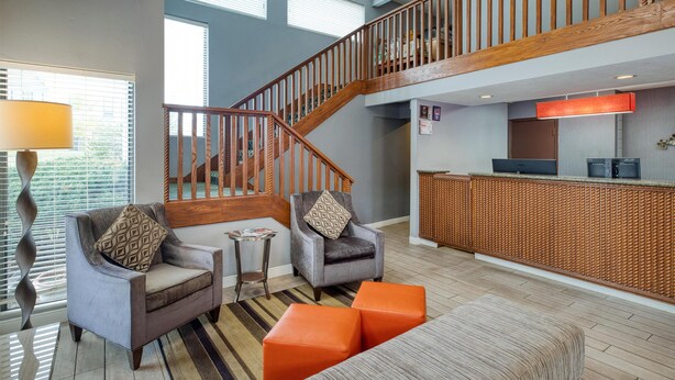 Un vestíbulo amplio con una escalera de madera, asientos cómodos y un mostrador de recepción.
