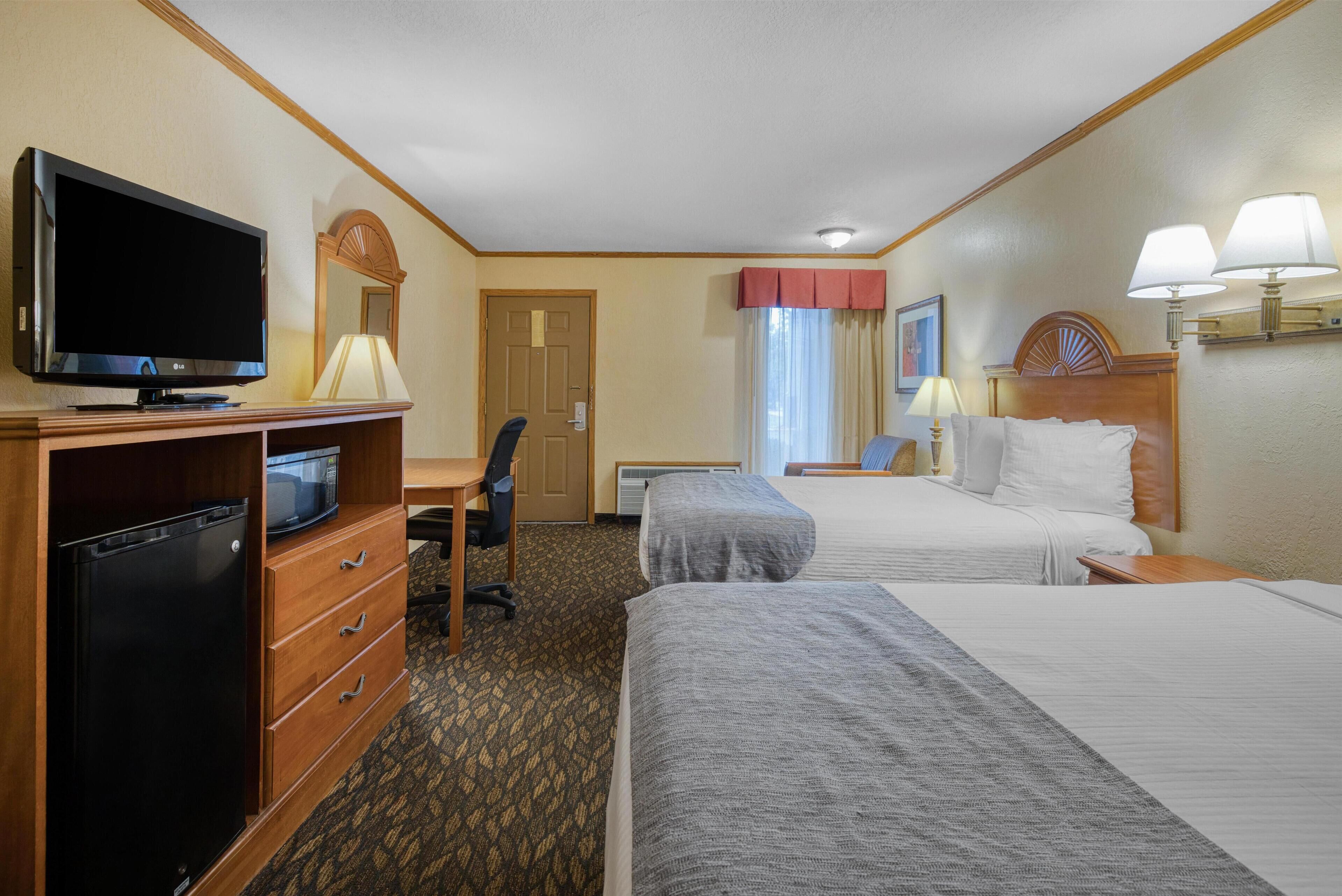 A hotel room with two beds, a desk, a television, and a refrigerator.