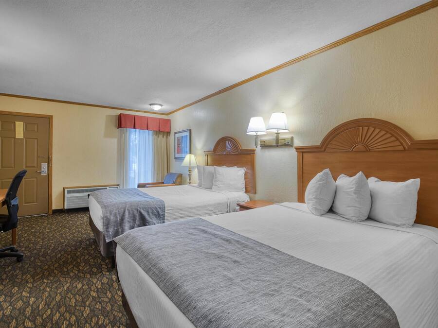 A hotel room with two beds, a desk, a chair, and a window with curtains.