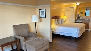 A hotel room with a bed, a chair, a small table, a lamp, and a microwave in the kitchenette. - Marina Inn (Des Moines)