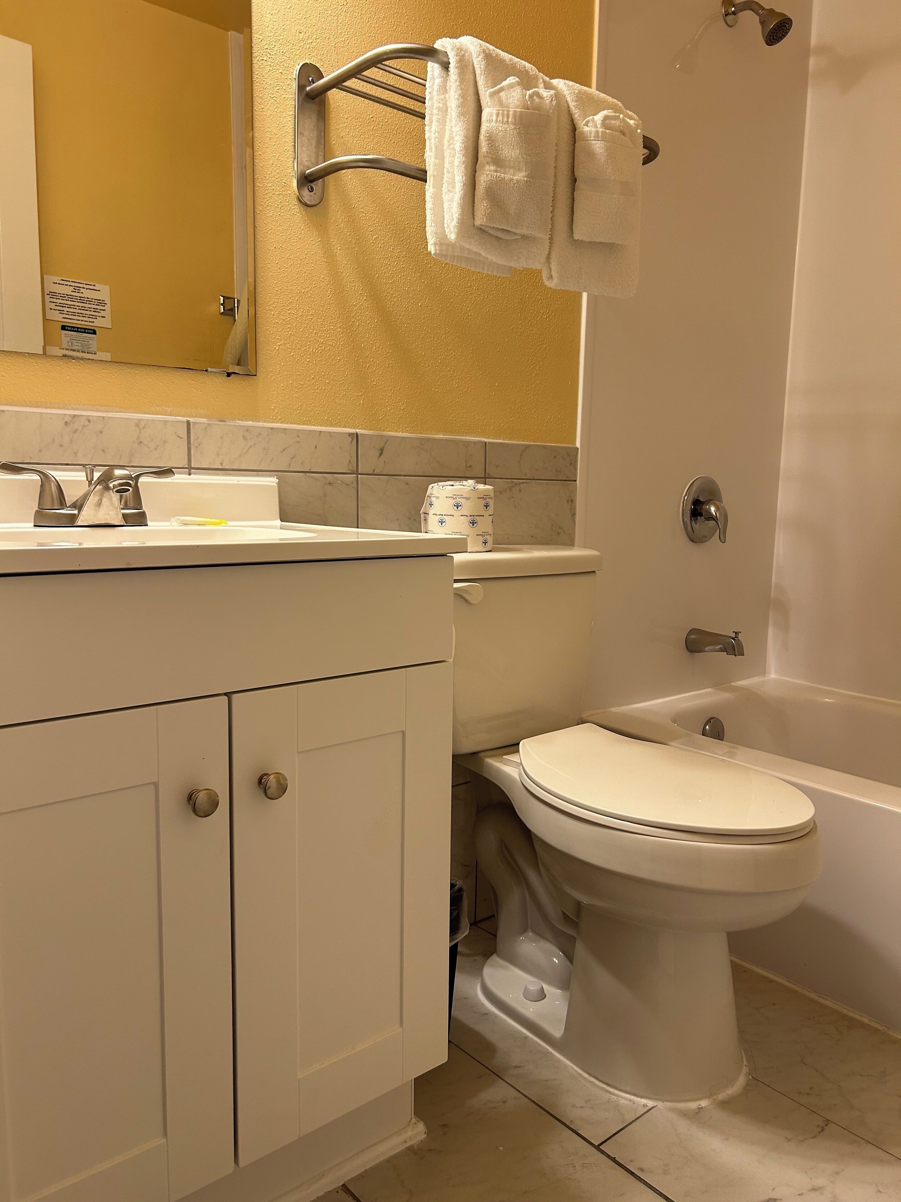 A bathroom with a white sink, toilet, and bathtub. There is a towel rack above the sink and a roll of toilet paper on the wall.