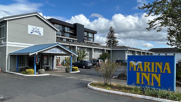 A Marina Inn with a blue and white exterior, a parking lot, and a clear sky. - Marina Inn (Des Moines)