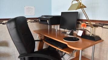 Une chambre d’hôtel avec un bureau en bois, une chaise de bureau noire, un ordinateur de bureau, une imprimante et une lampe de bureau.