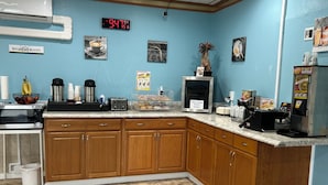 A breakfast room with a digital clock, coffee maker, toaster, and a sign indicating cream cheese, butter, and yogurt are available. - Marina Inn (Des Moines)