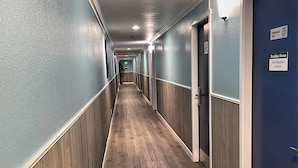 A long, narrow hallway with wooden flooring and blue walls, featuring doors on both sides and a sign indicating a breakfast room and fire monitor system. - Marina Inn (Des Moines)