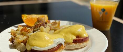 A plate with eggs benedict, hash browns, and a glass of orange juice on a table.