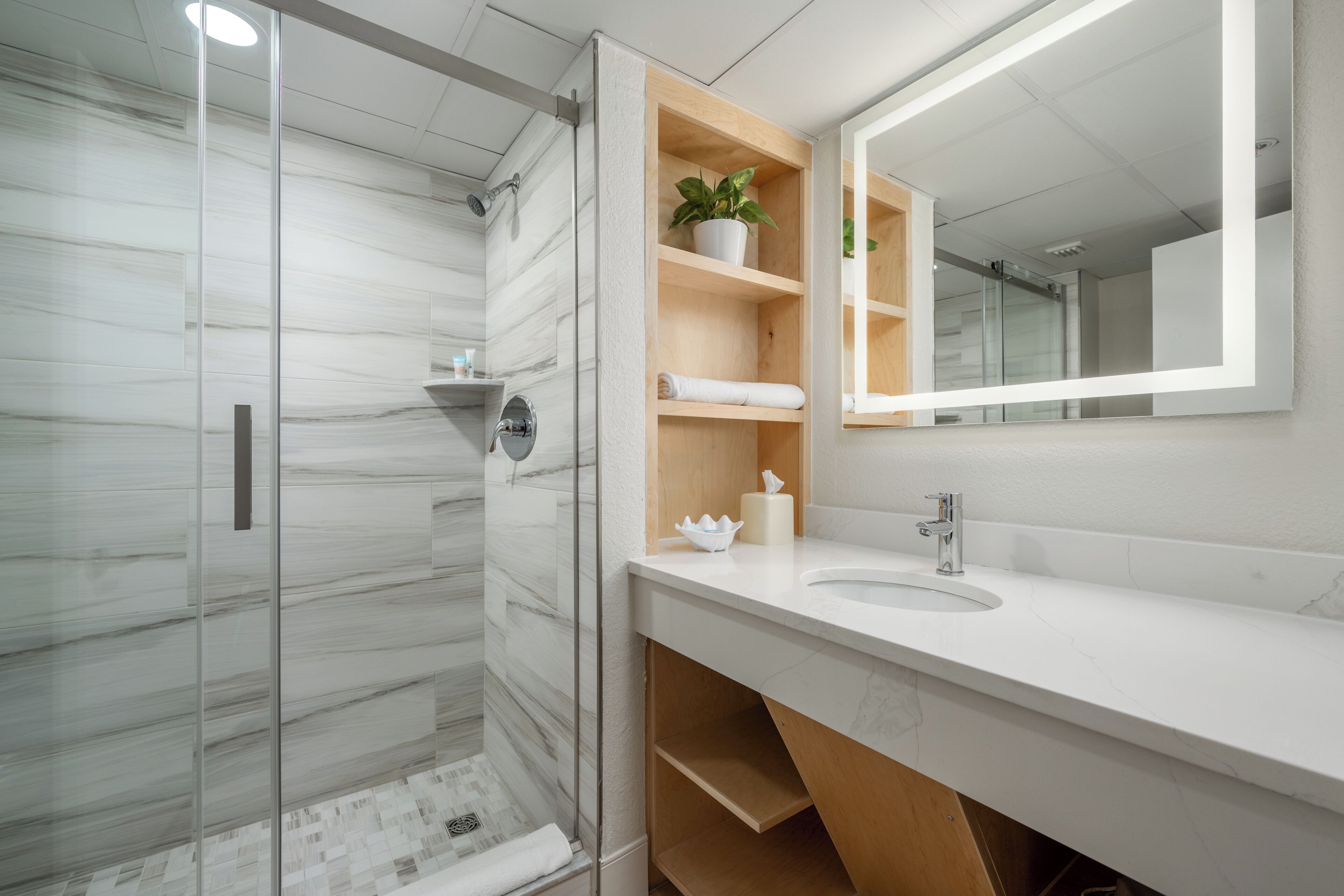 Un baño moderno con cabina de ducha de vidrio, lavamanos blanco y tocador de madera.