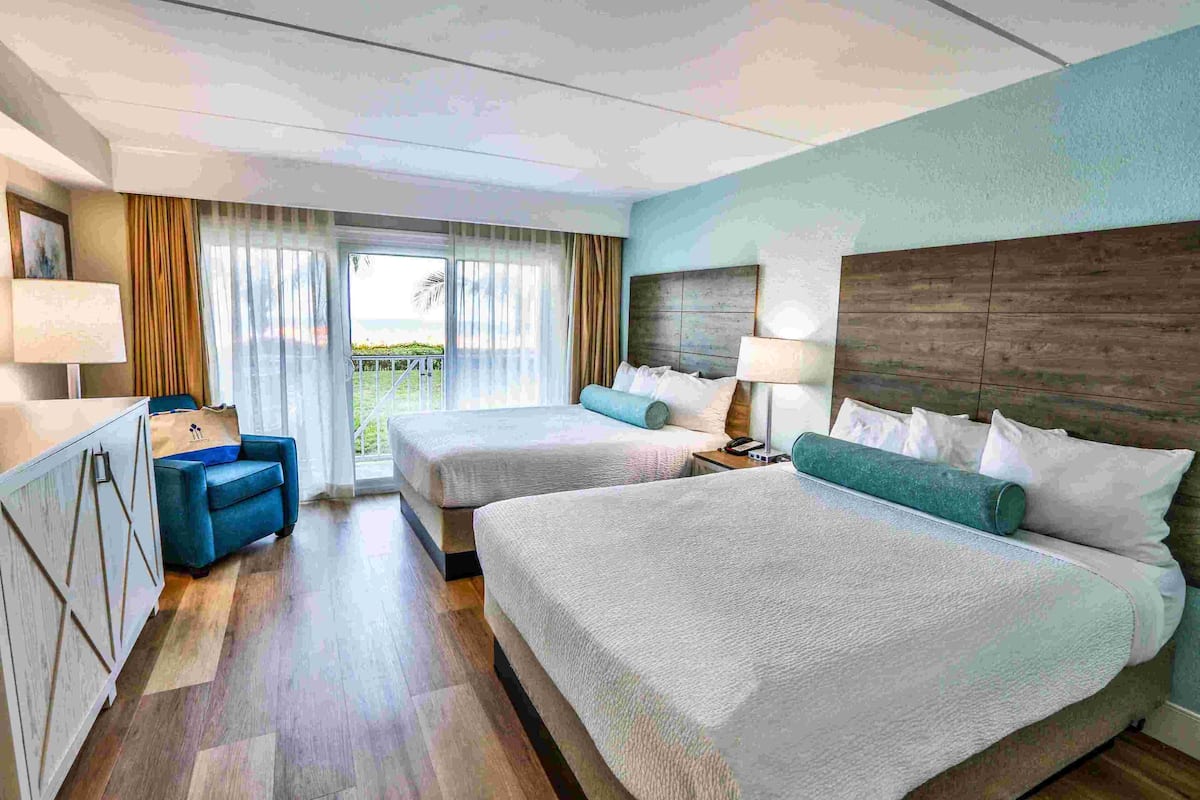 A hotel room with two beds, a sofa, a desk, and a view of the outdoors.