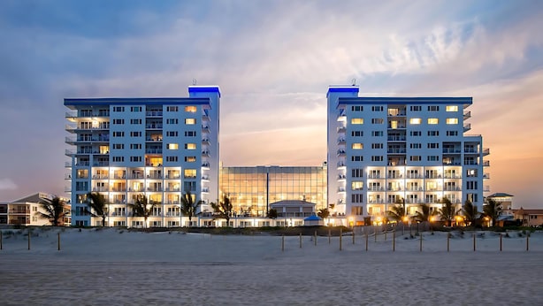 A beachfront hotel with multiple floors, balconies, and a large glass facade.