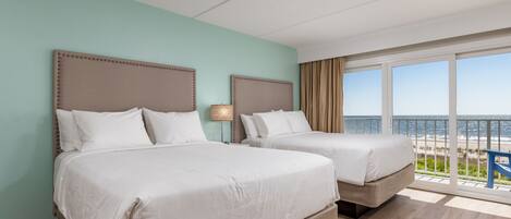 Une chambre d’hôtel avec deux lits, une grande fenêtre donnant sur la plage et un balcon avec une chaise bleue.