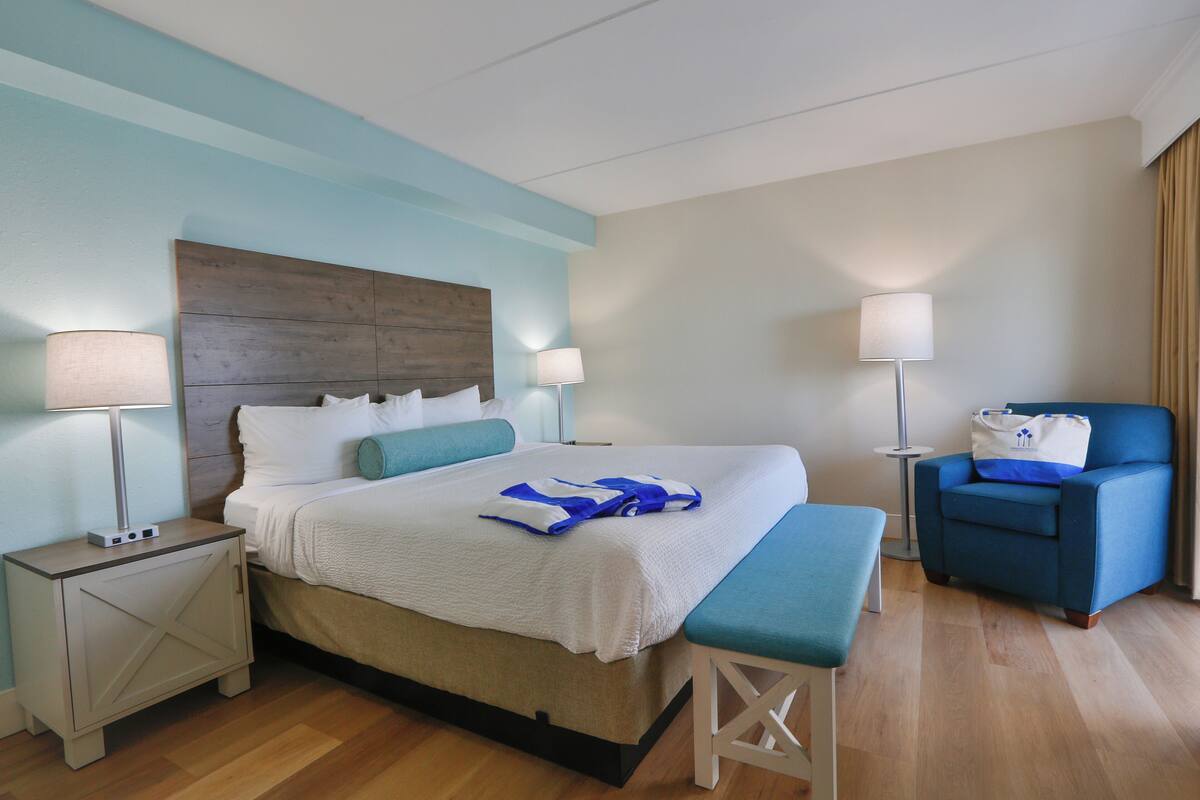 A hotel room with a bed, bedside tables, a bench, a chair, and a lamp.