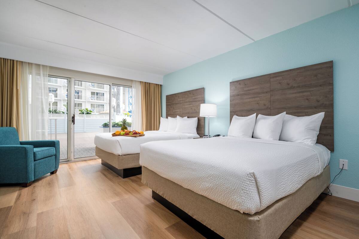 A hotel room with a large bed, a smaller bed, a sofa, and a dining table with fruit.