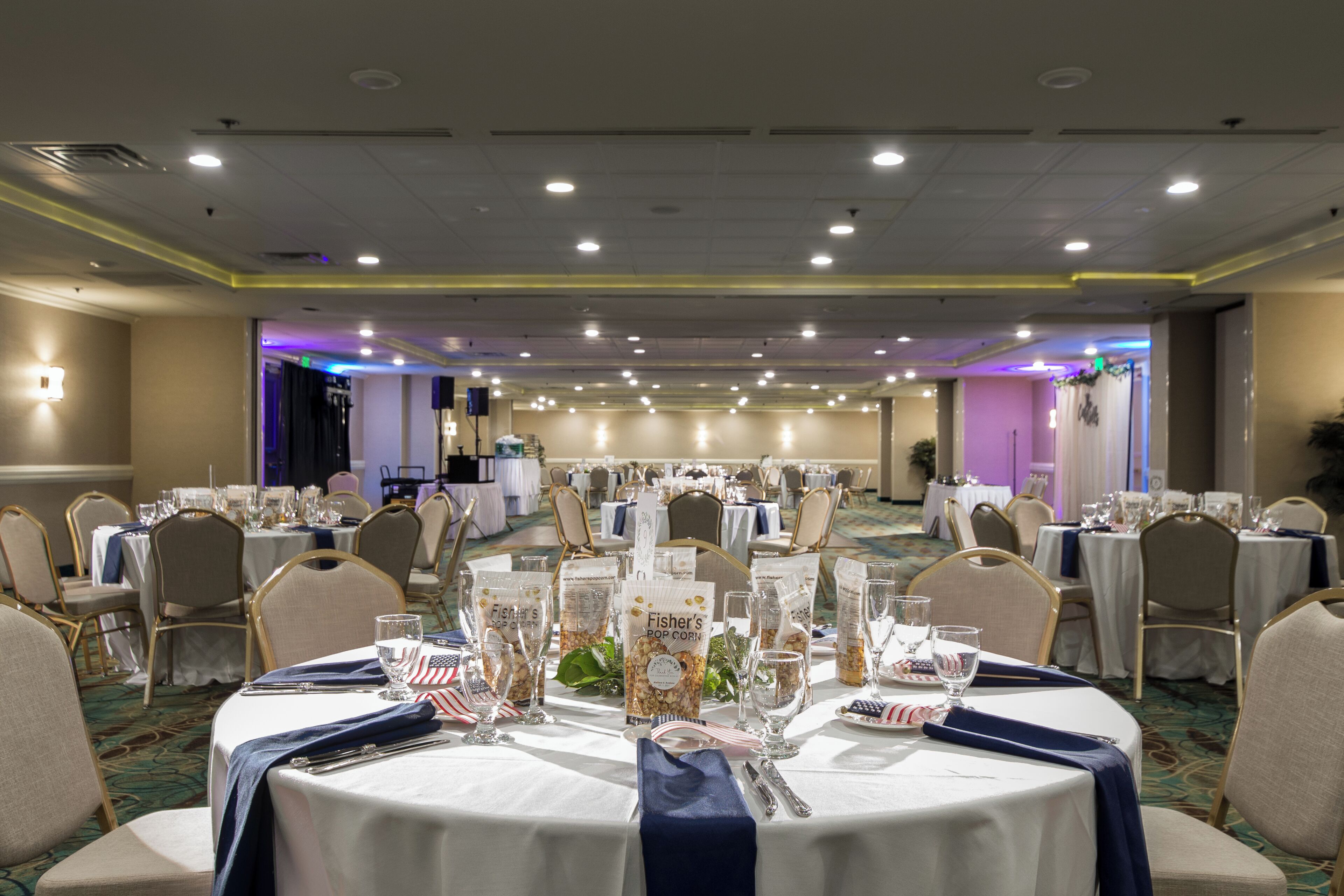 A banquet hall with round tables set for a formal event, featuring white tablecloths, blue napkins, and American flag decorations.
