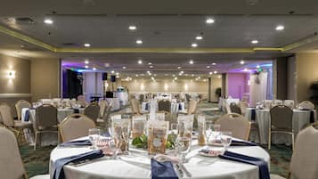 A banquet hall with round tables set for a formal event, featuring white tablecloths, blue napkins, and American flag decorations.