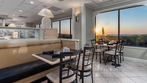 A restaurant with a high ceiling, large windows, and a view of the sunset.