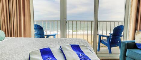 Une chambre d’hôtel avec un lit, deux chaises bleues, une table et une vue sur la plage.