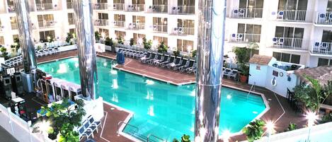 A hotel pool with multiple levels of balconies, lounge chairs, and potted plants.