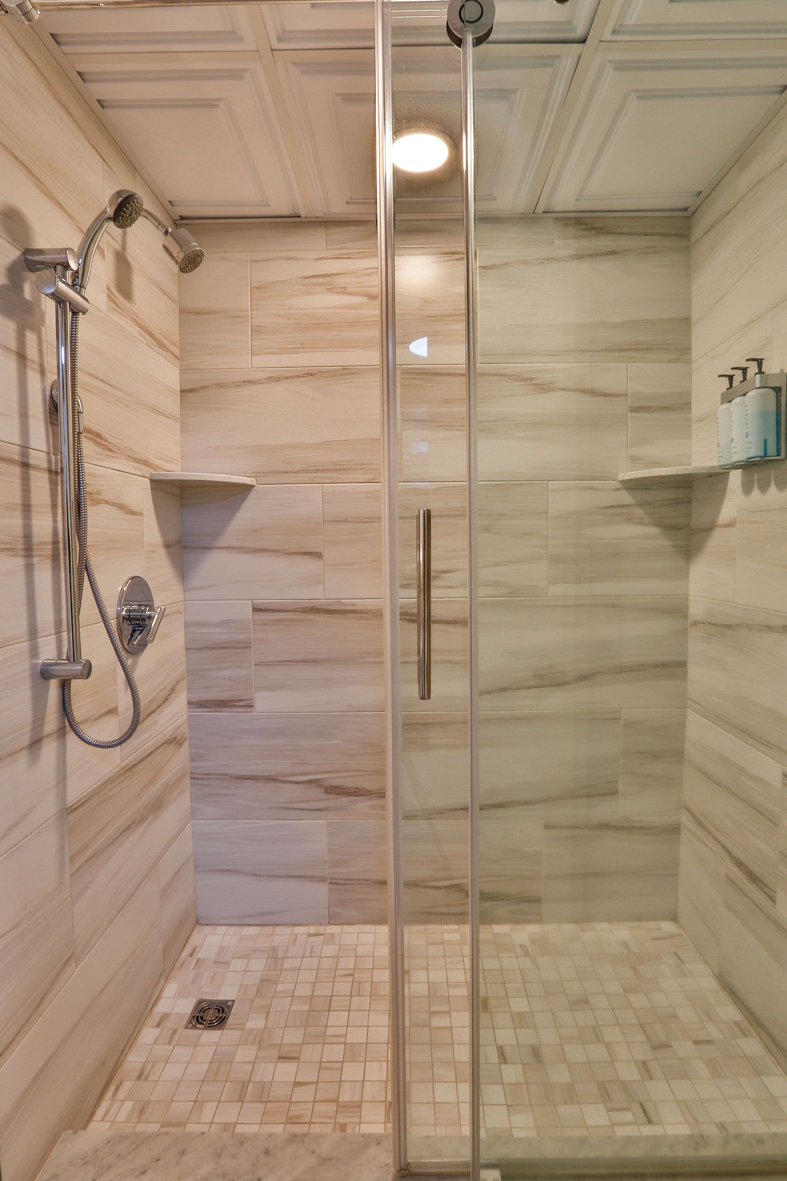A glass-enclosed shower with a handheld showerhead and a wall-mounted faucet.