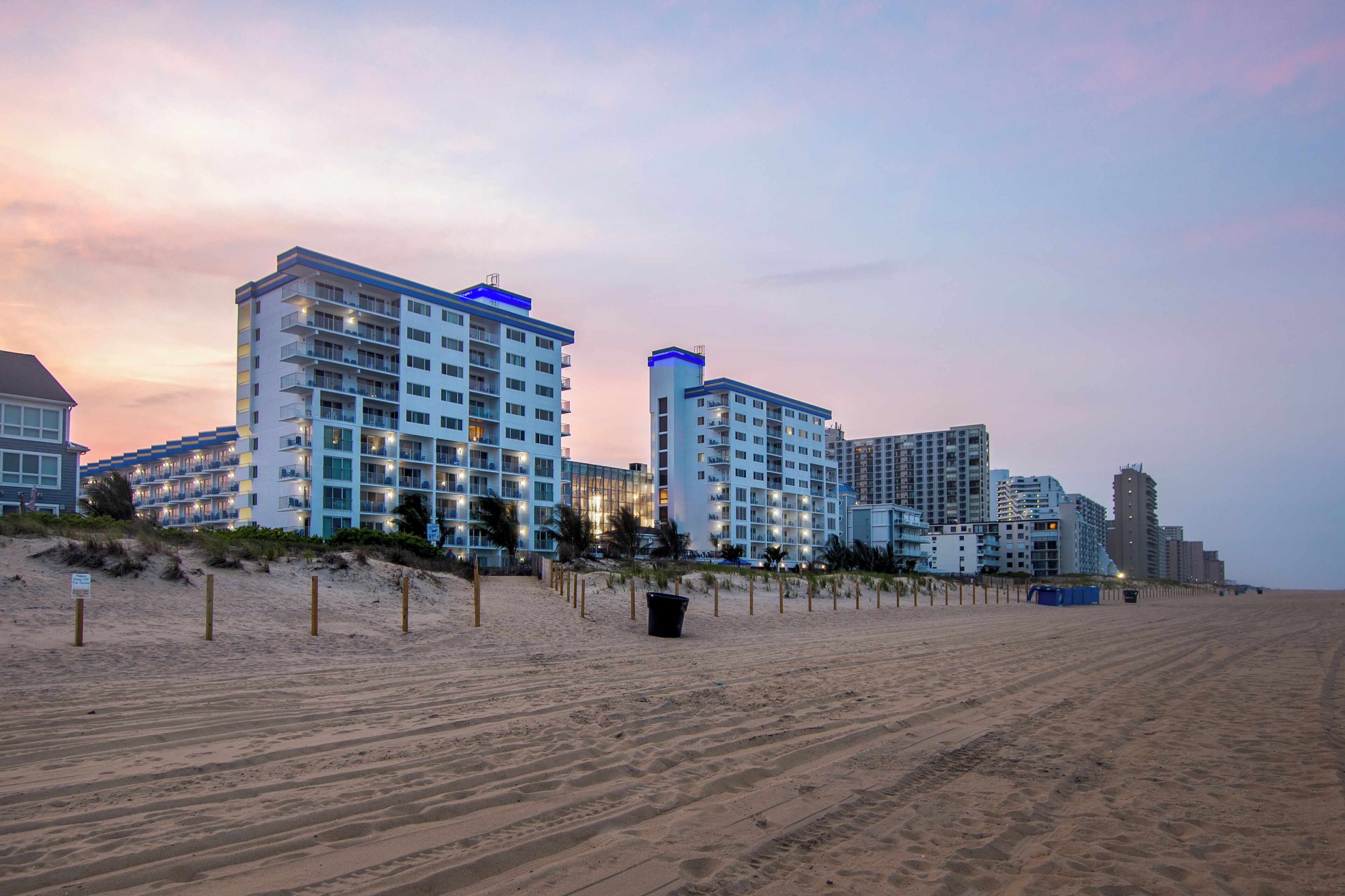 Un hotel frente a la playa con varios edificios de gran altura, una playa de arena y cielo despejado.