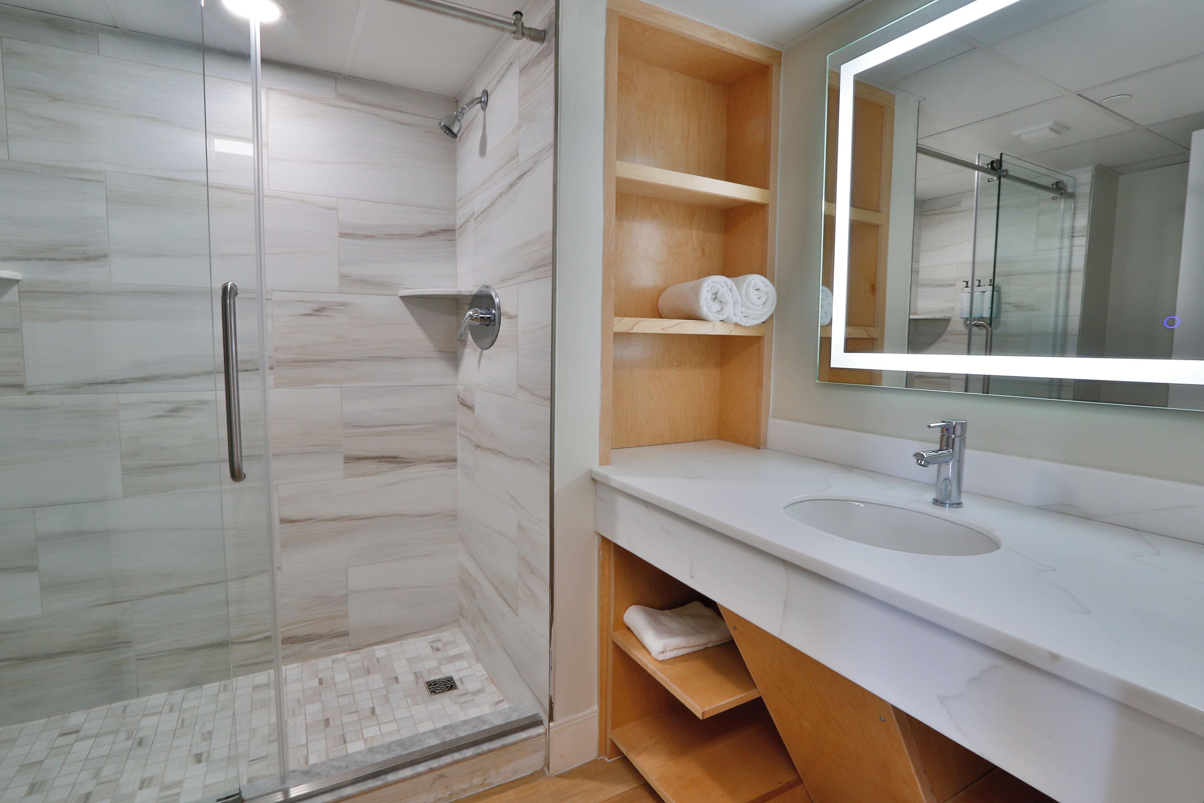 A modern bathroom with a glass-enclosed shower, a white sink, and a wooden vanity.