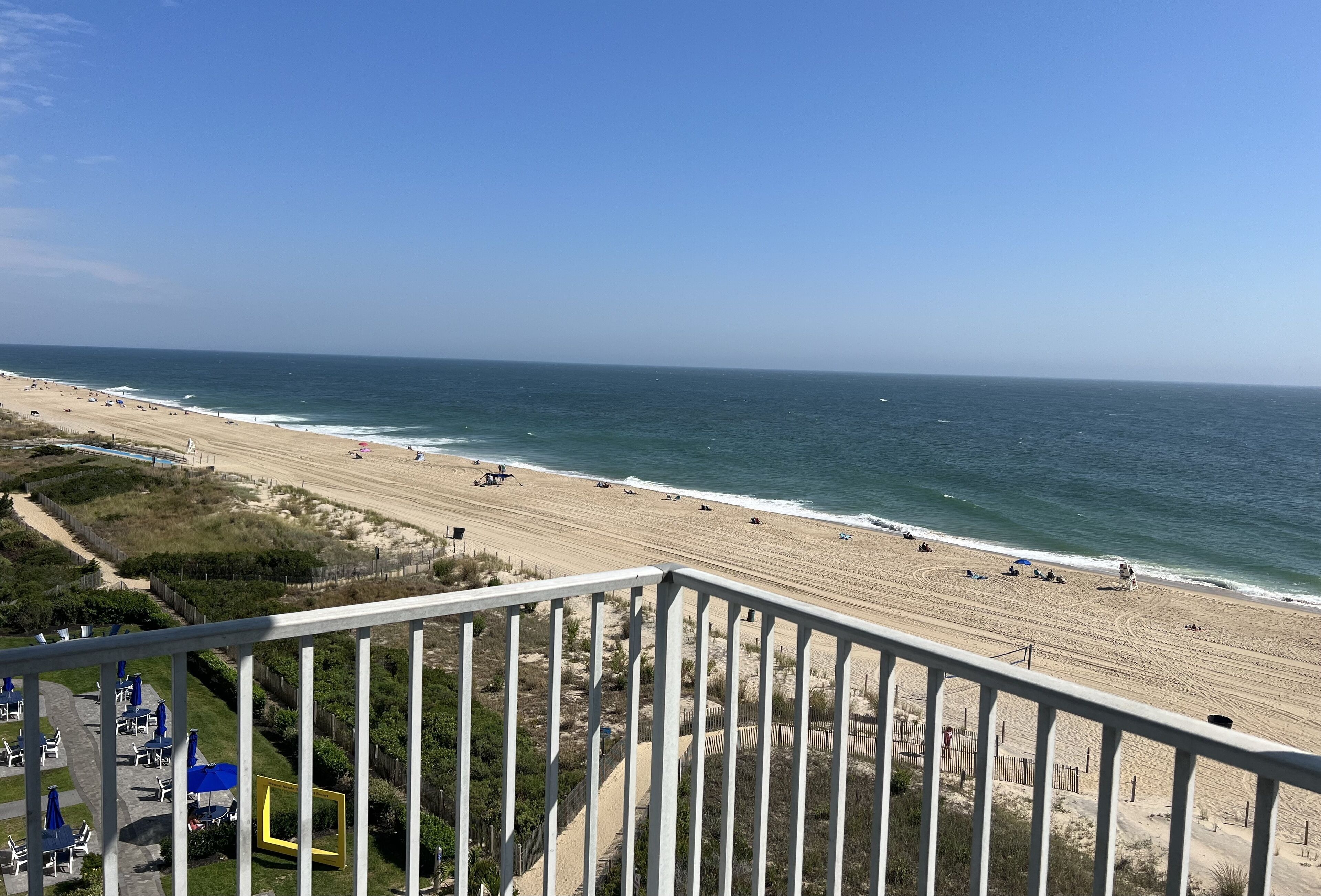 A beach with a clear view of the ocean and a fenced area with beach chairs and umbrellas.