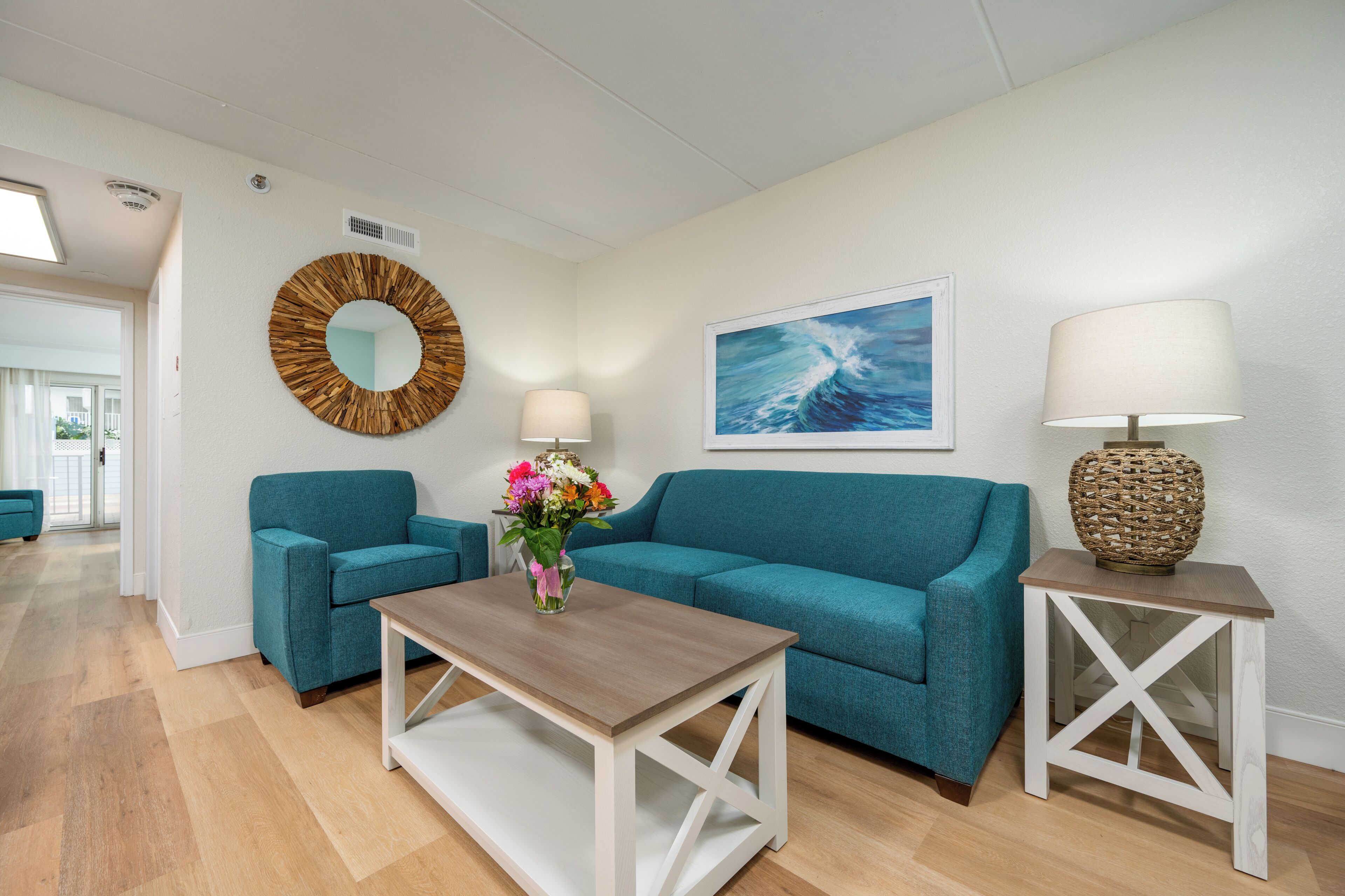A modern living room with teal sofas, a wooden coffee table, and a white side table with a lamp.
