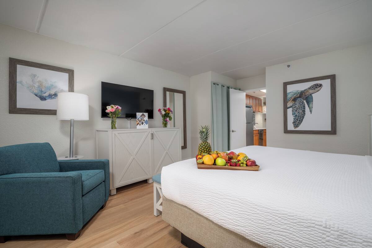 A hotel room with a bed, a sofa, a TV, and a fruit tray on the bed.