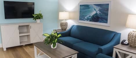 Una sala de estar con un sofá azul, un televisor, una lámpara y un cuadro de una ola.
