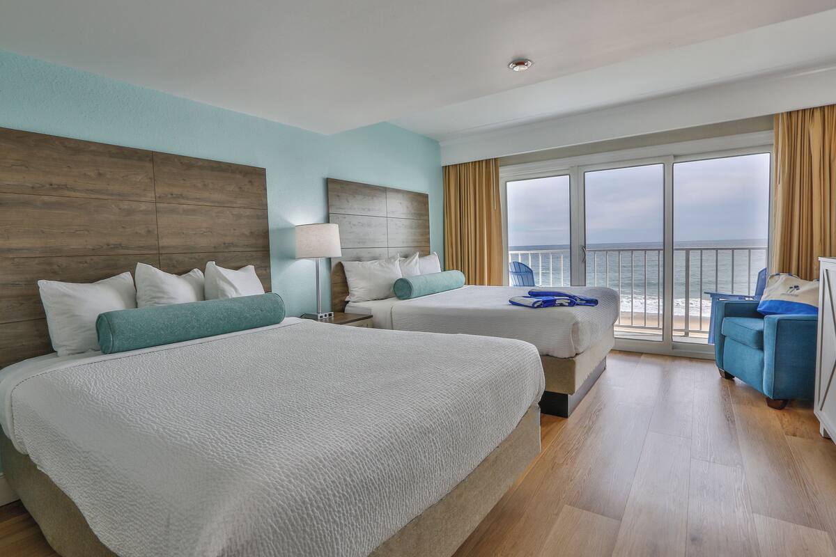 A hotel room with two beds, a balcony with a view of the sea, and a blue armchair.