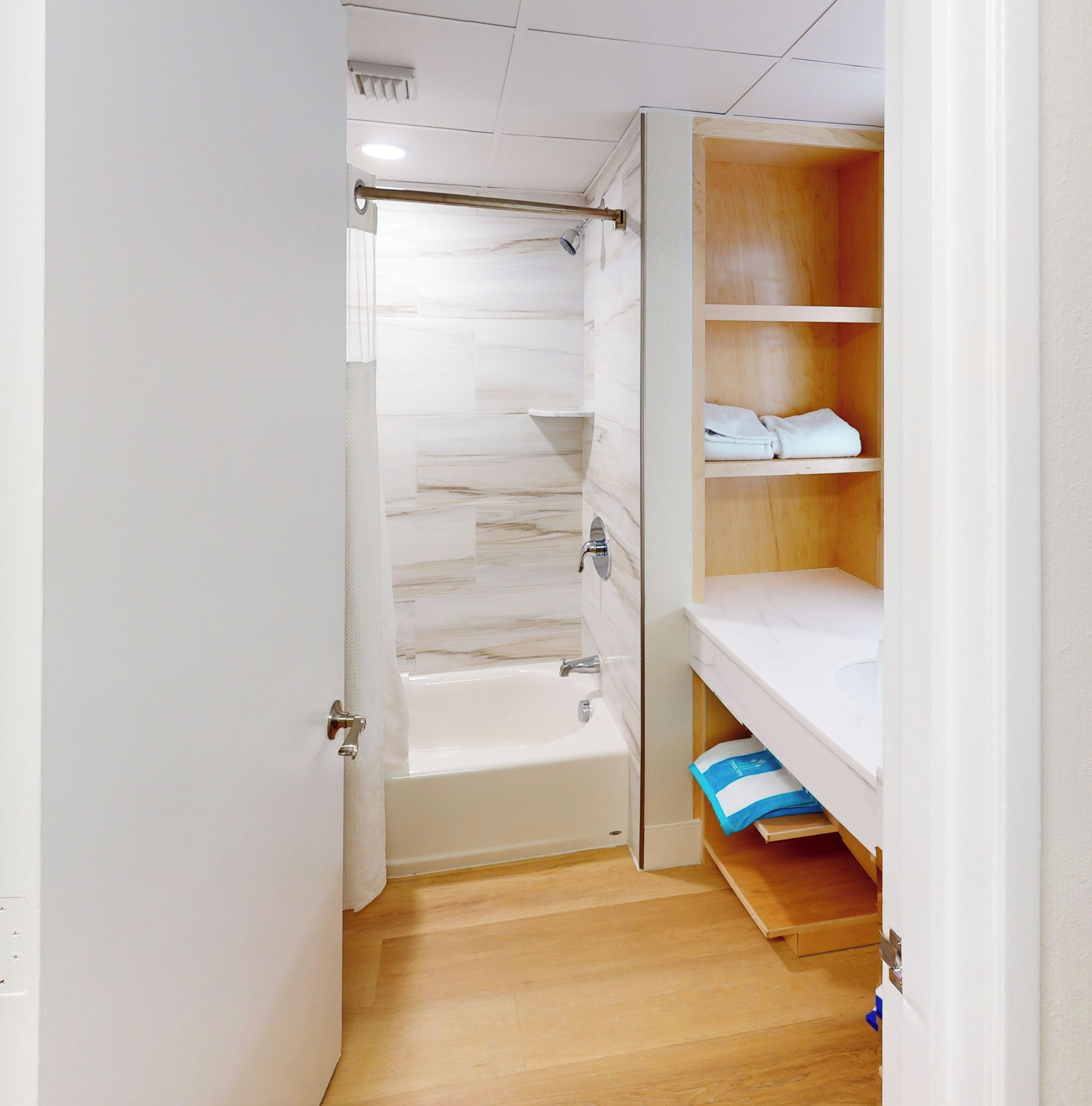 A bathroom with a bathtub, a shower, and a wooden shelf with towels.