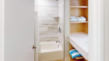 A bathroom with a bathtub, a shower, and a wooden shelf with towels.
