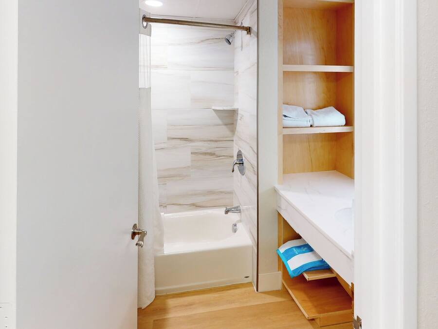 A bathroom with a bathtub, a shower, and a wooden shelf with towels.